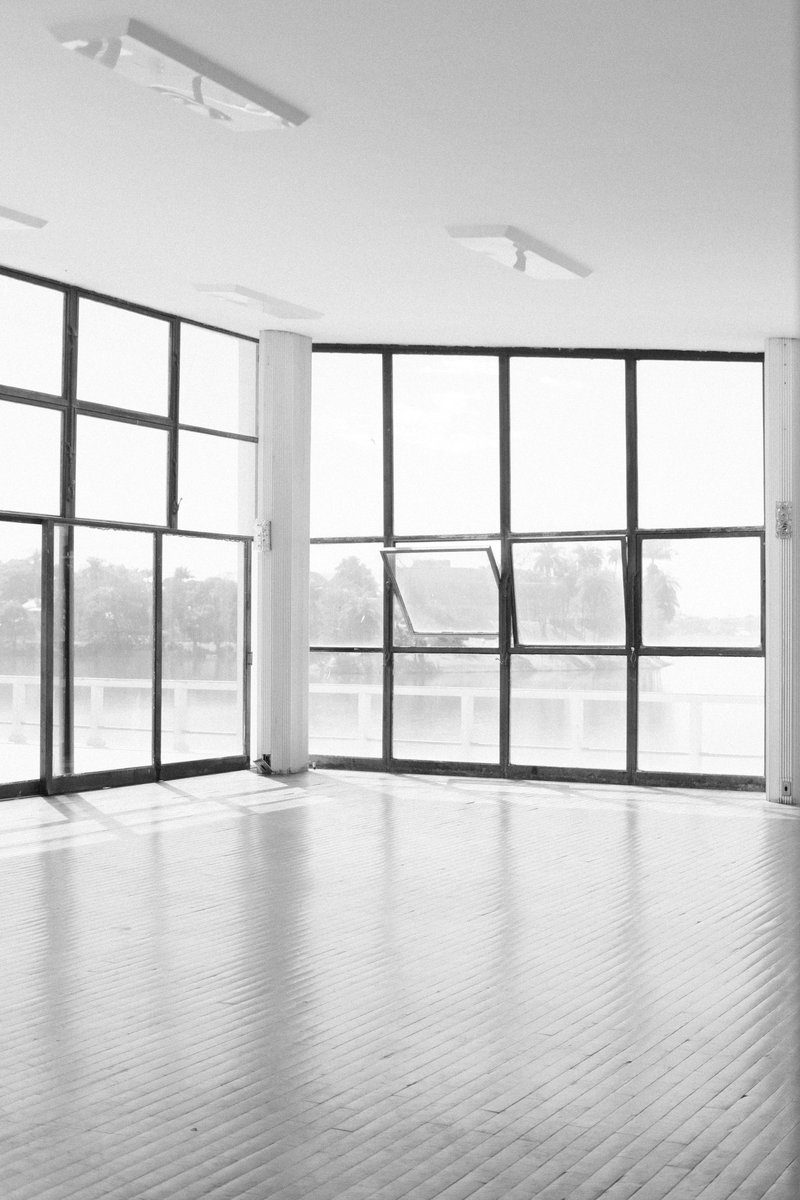 Salle vide photographiée en noir et blanc, éclairée par de grandes fenêtres