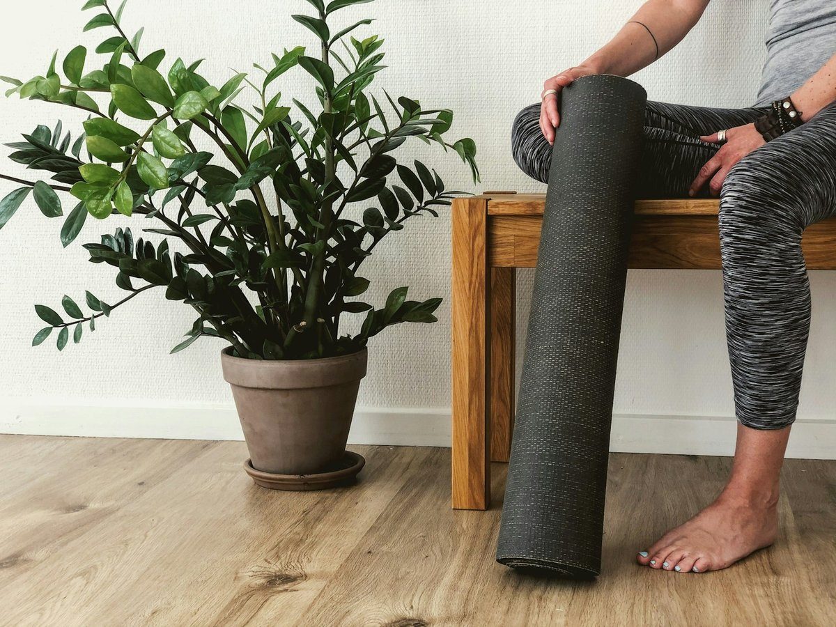 Personne assise tenant à la main un tapis d'exercice roulé, visage hors du cadre